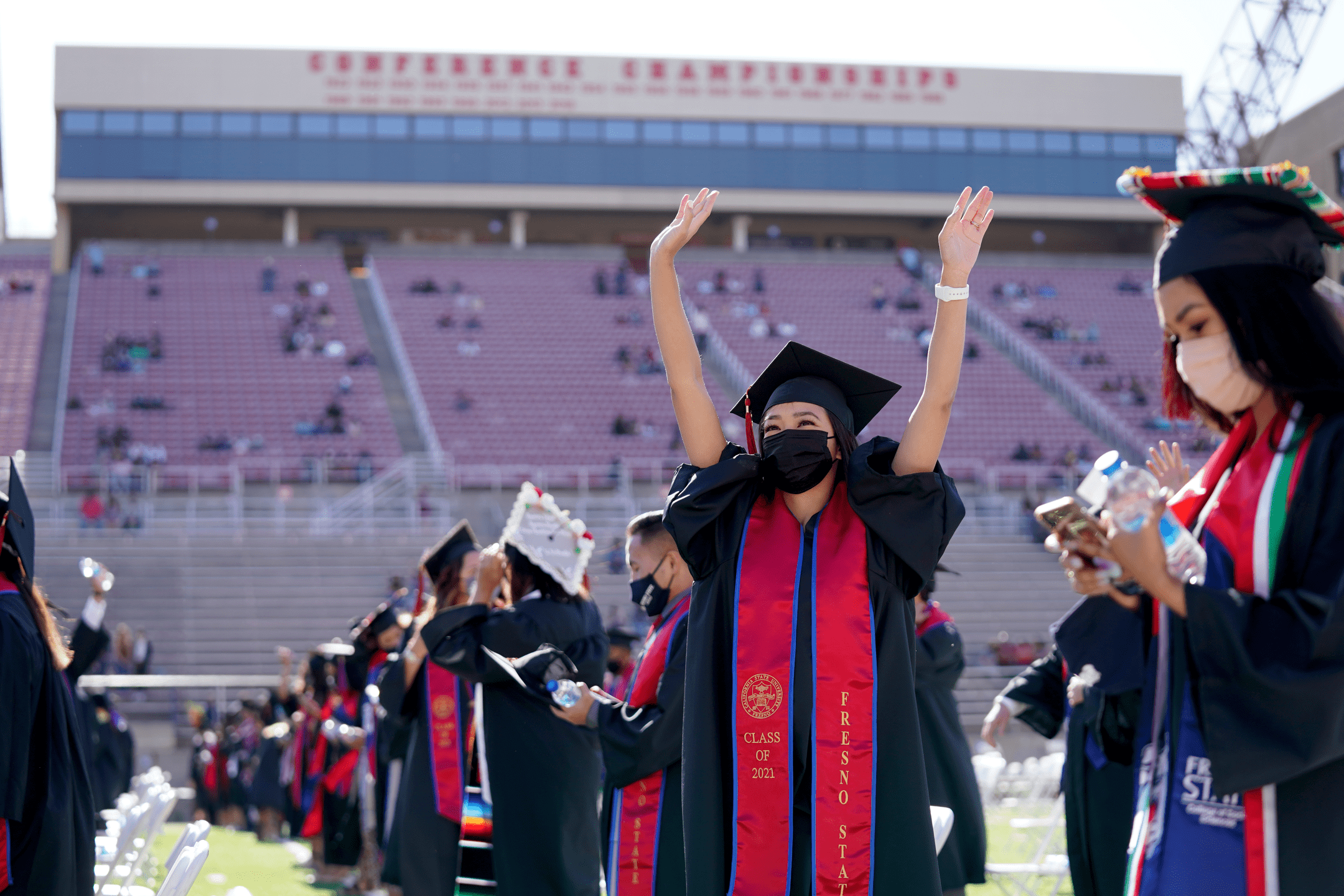 Student with mask and arms raised at graduation