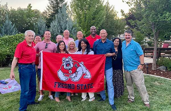 A group of alumni hold up a red Fresno State Bulldogs flag at an event as part of the southern California professional network.